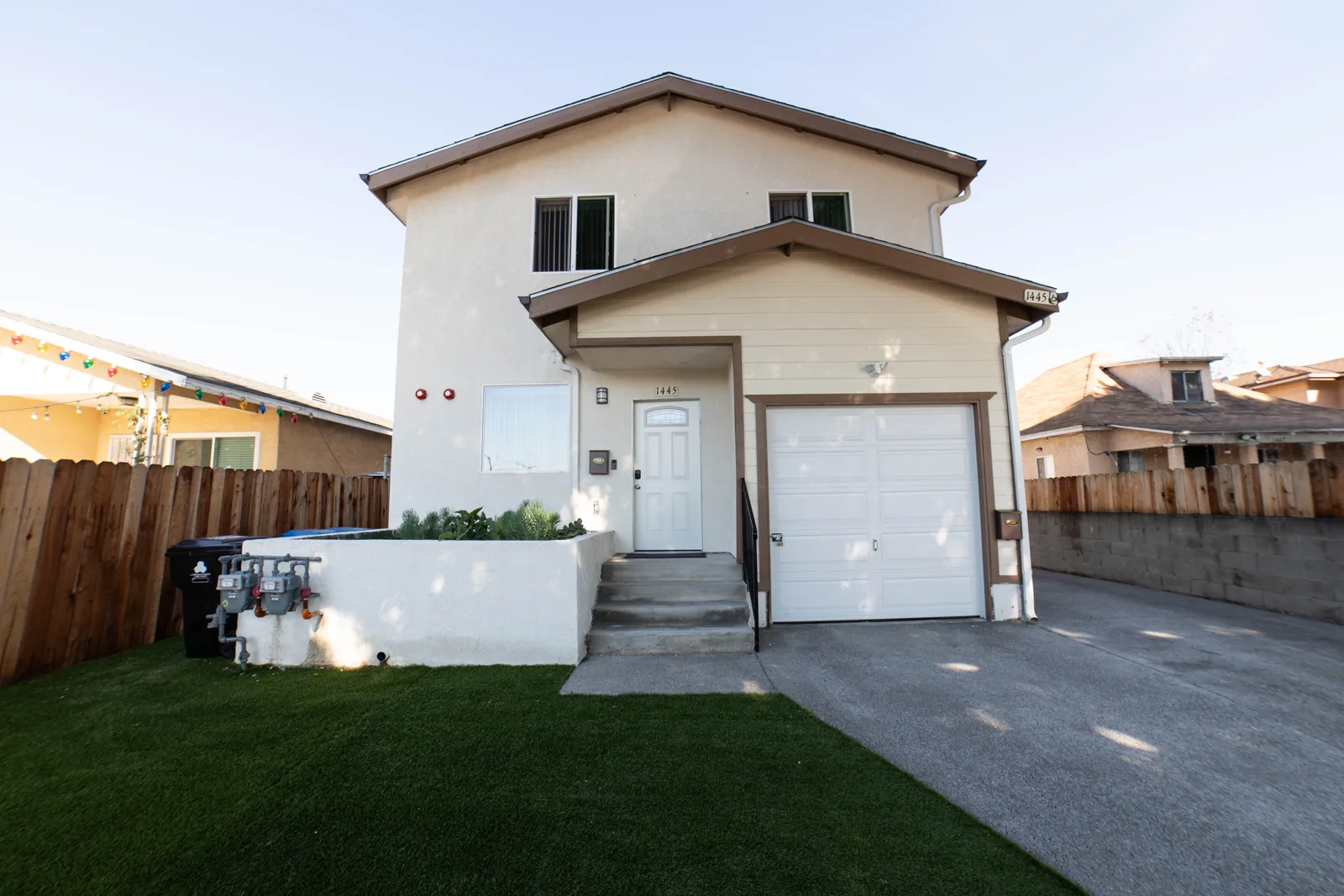 Front of the Wellness Housing home on East 54th Street in Los Angeles with its attached garage and front lawn