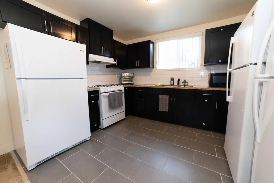 Shared kitchen on East 54th Street with a gas range two full size refrigerators and dark cabinets