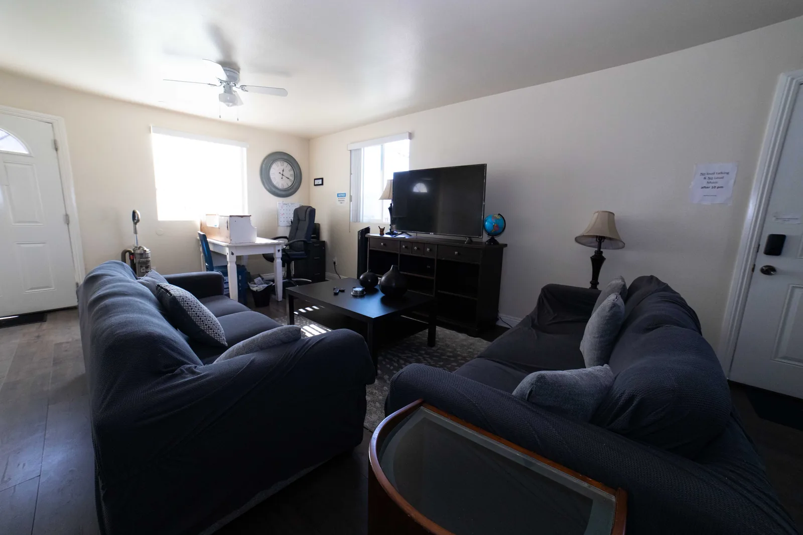 Common room on West 42nd Street with two sofas a television a ceiling fan and a shared desk