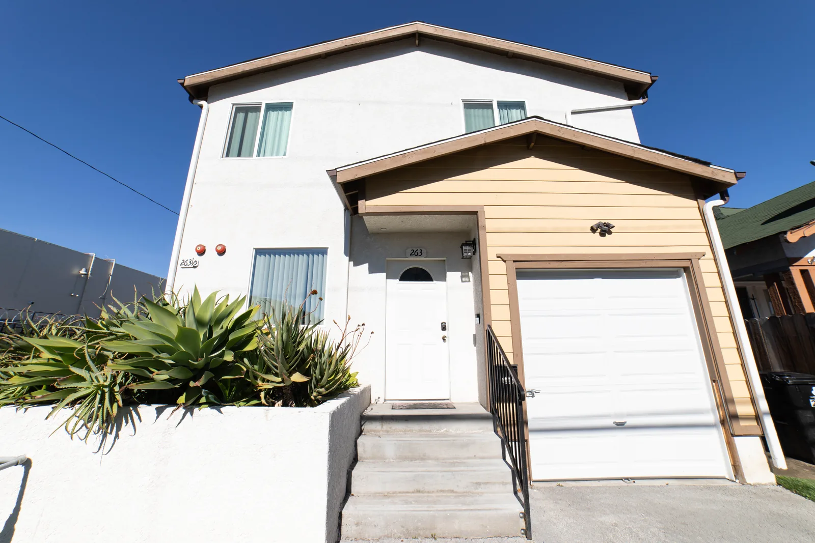 Front of the Wellness Housing home on West 42nd Street in Los Angeles with its entry steps and garage