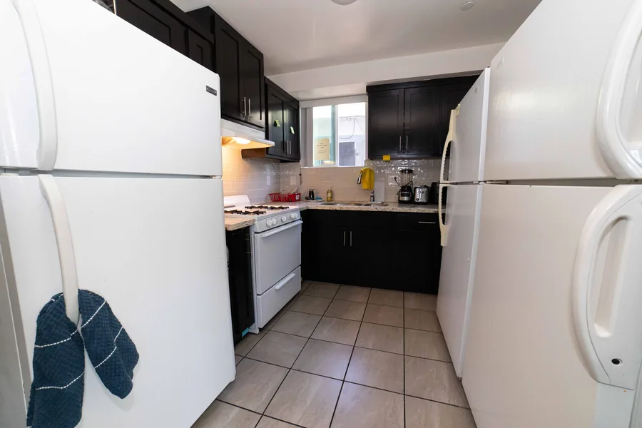 Shared kitchen at the West 42nd Street house with two refrigerators a gas range and a tiled floor