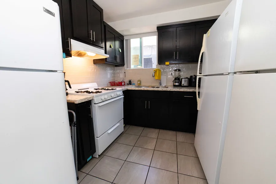 Wide view of the shared kitchen on West 42nd Street with dark cabinets and a full size refrigerator