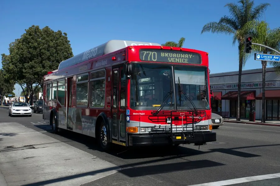 A red Los Angeles Metro Rapid bus pulling through an intersection on a palm lined street
