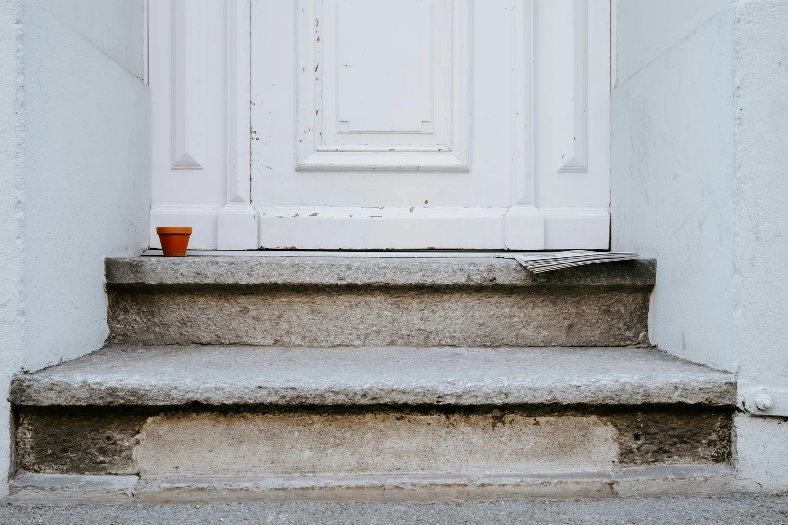 A plain white front door at the top of three worn concrete steps