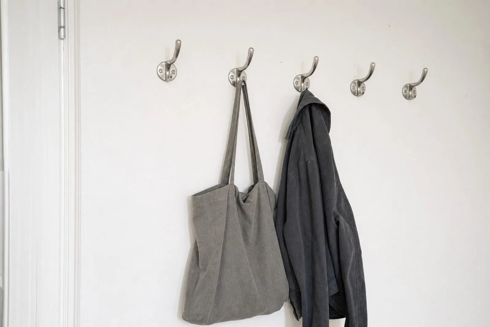 A row of coat hooks on a wall holding a canvas tote bag and a jacket