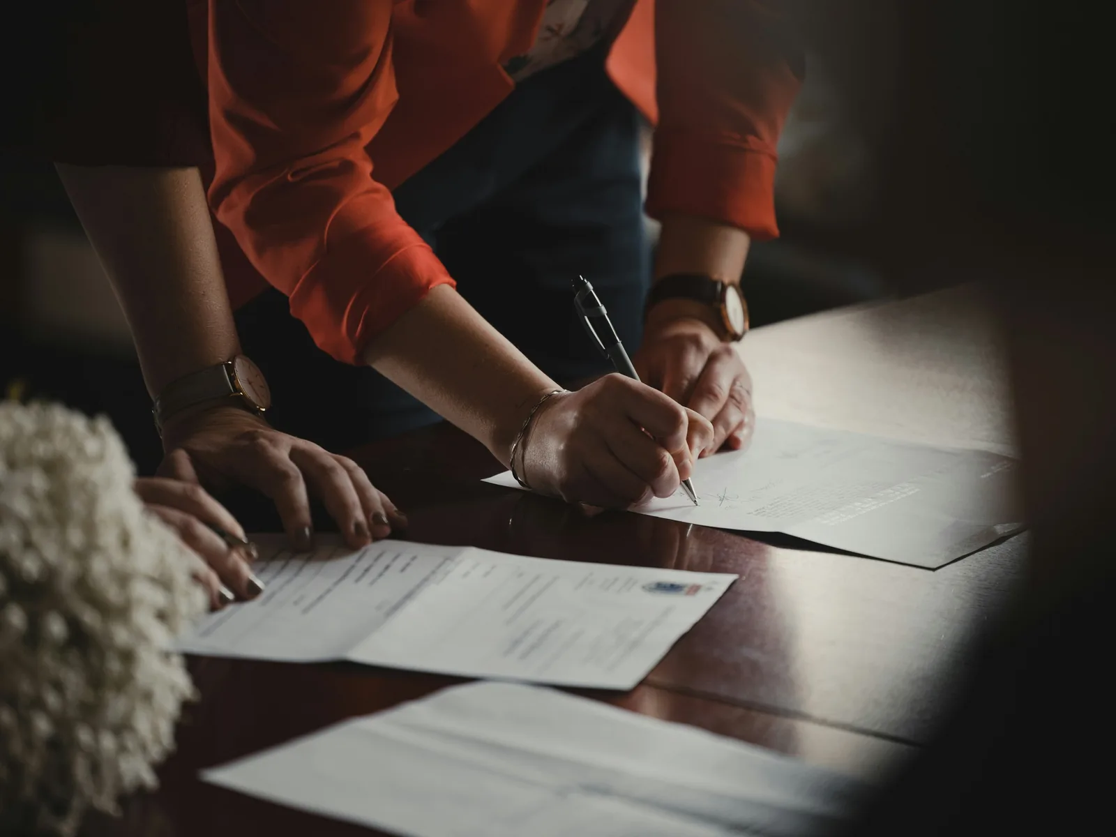 Two people filling in paperwork on a table, seen from above the hands